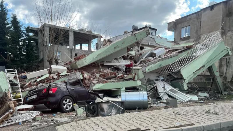 The aftermath of the devastating earthquake, showing collapsed buildings and a crushed car.