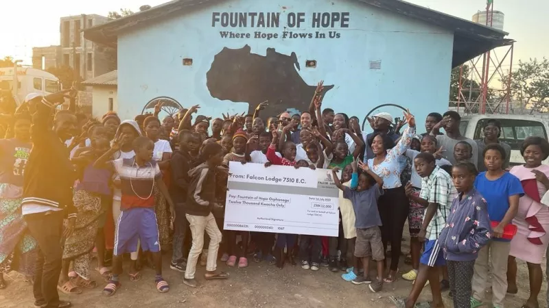 Children standing outside the Fountain of Hope orphanage in Zambia with a donation cheque from Zambian Freemasons.