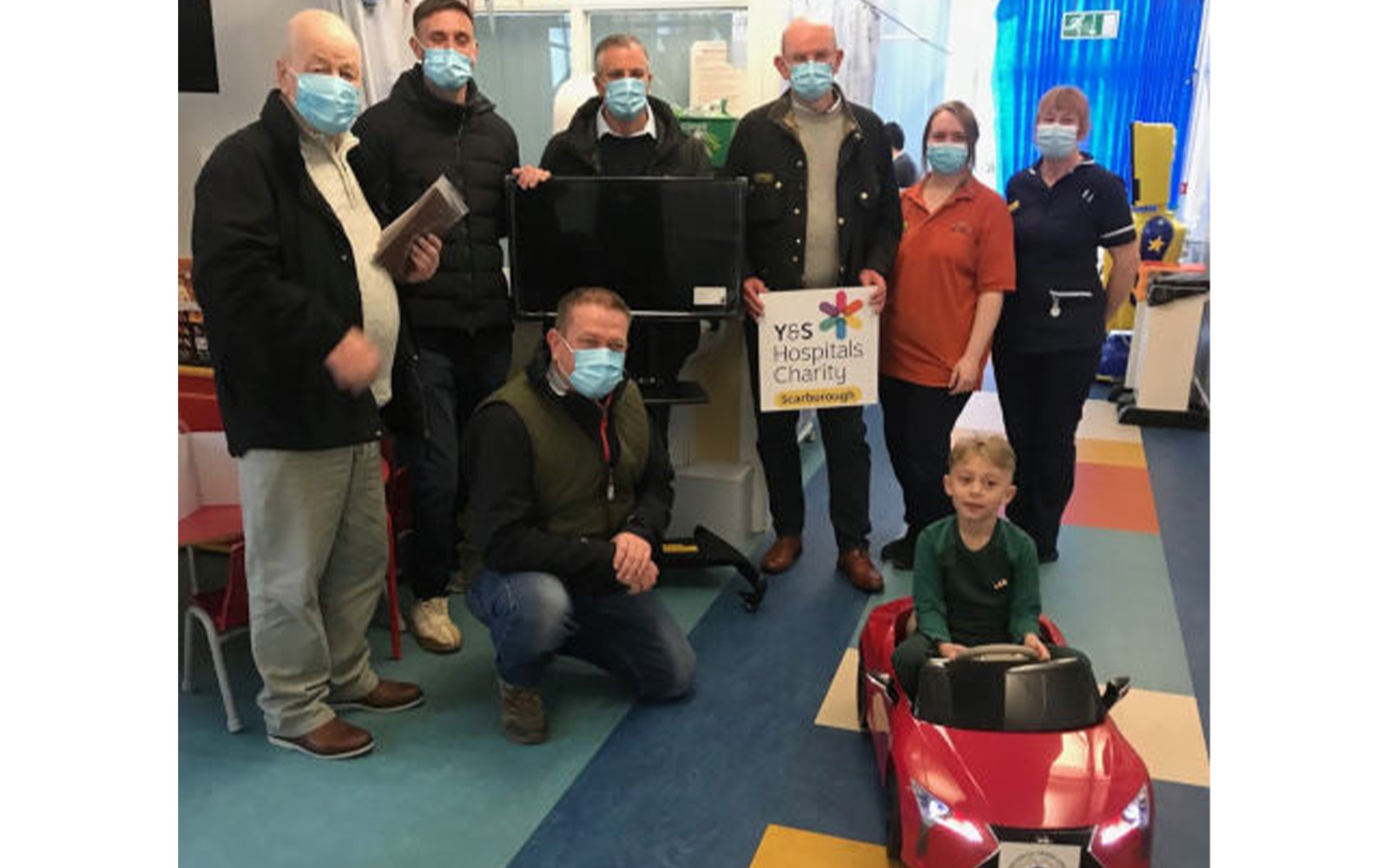 joseph in a red battery powered car, with hospital staff and members of donating lodges