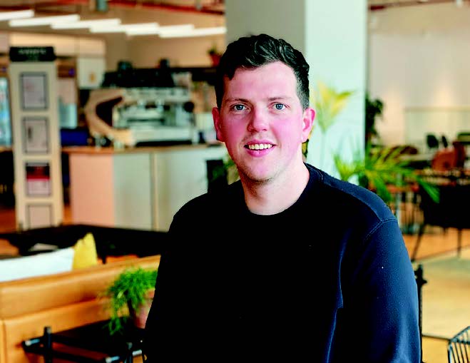 Ollie Coburn is a wearing a navy jumper and is smiling at the camera.