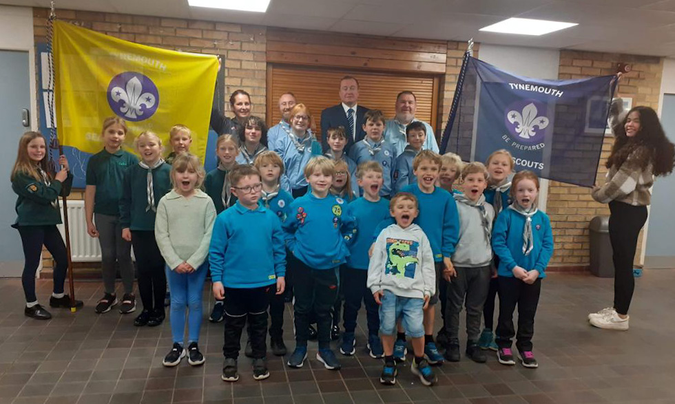 A group of Sea Scouts proudly holding up ther new banners. The banners are two flags, one yellow, one blue. Bother have the Sea Scouts logo on.