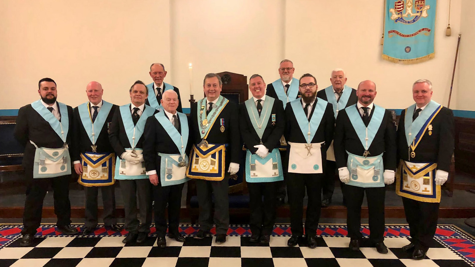 The lodge stands in a group wearing full regalia on a checkerboard floor.