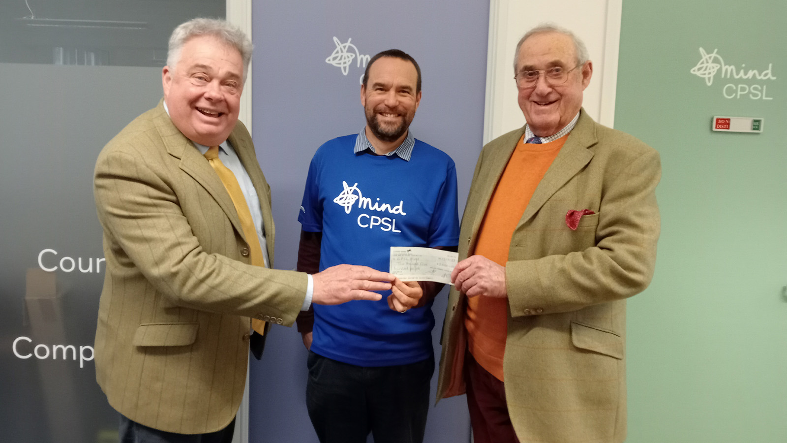 Two men stand either side of a Mind representative. All are holding the cheque and smiling.