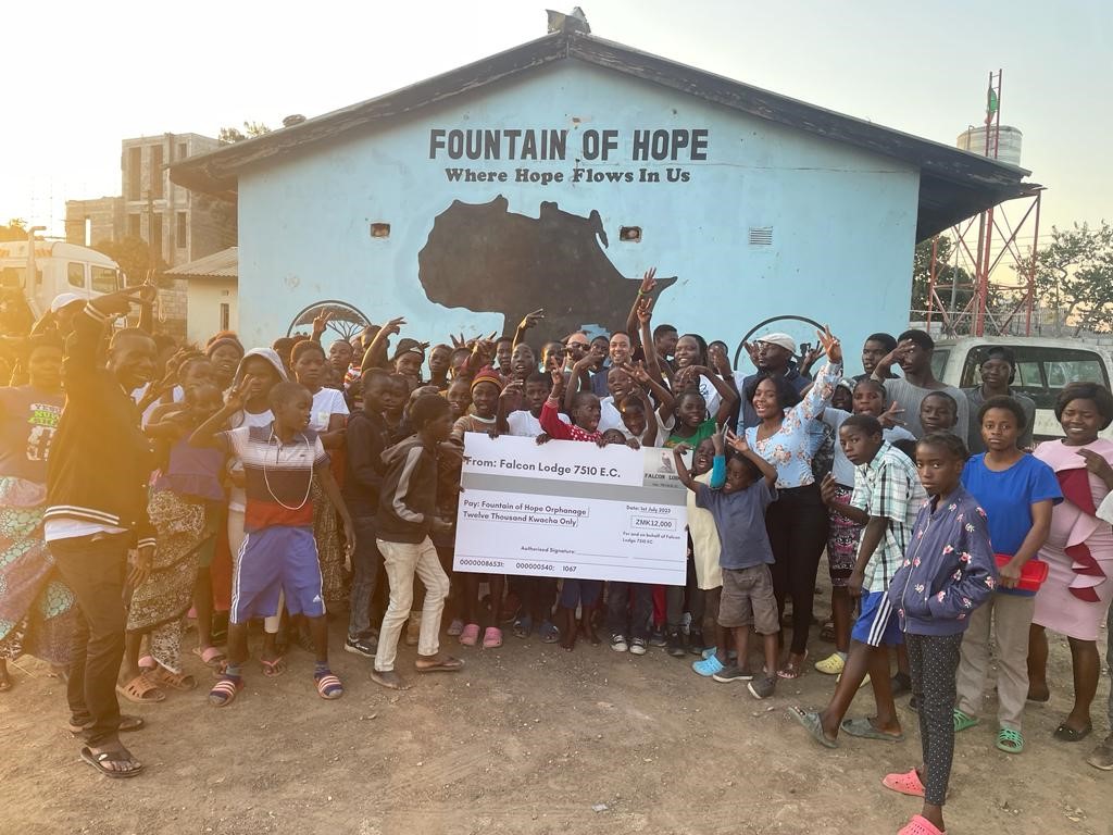 Children standing outside the Fountain of Hope orphanage in Zambia with a donation cheque from Zambian Freemasons.