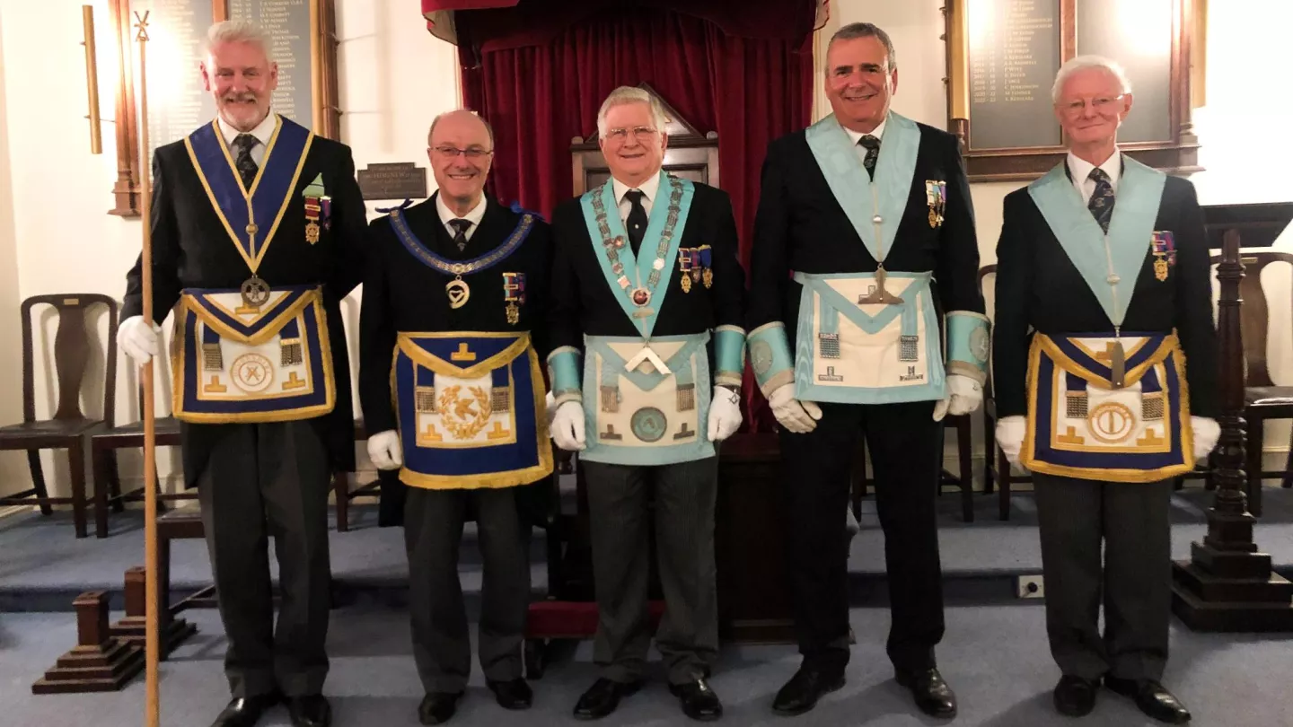 A group of Freemasons stand in a line each holding a plaque