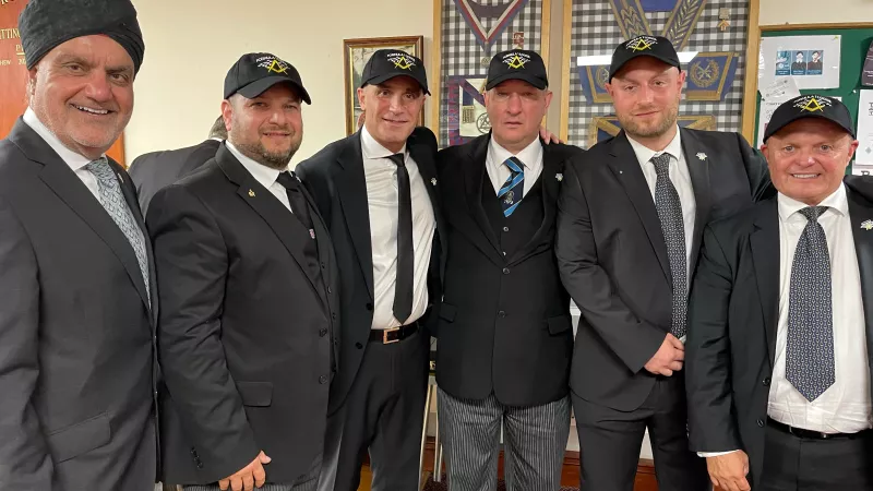 Freemasons standing together in suits, wearing distinctive formula one hats