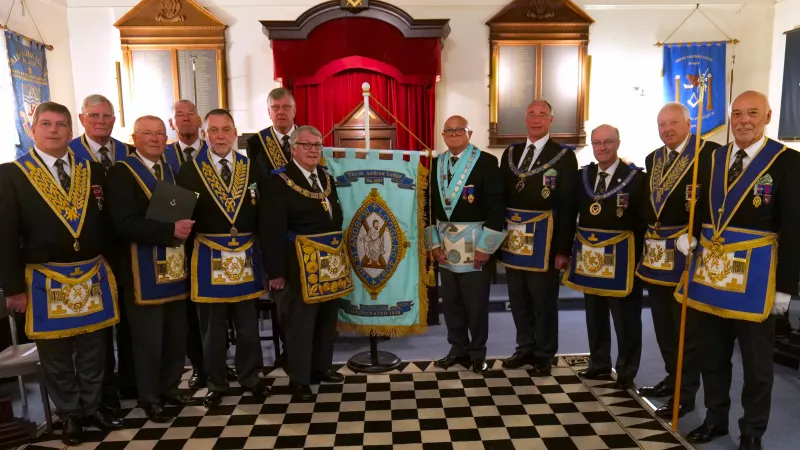 A group of Freemasons stand in a curved line either side of the St Andrews Lodge Banner