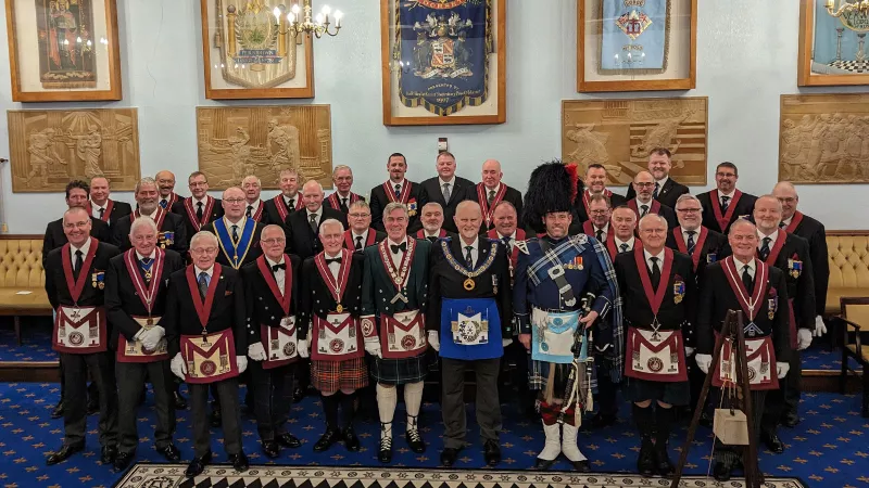 The Kenneth Cross Lodge stand in full regalia with George Moss and a piper wearing wearing traditional highland dress.