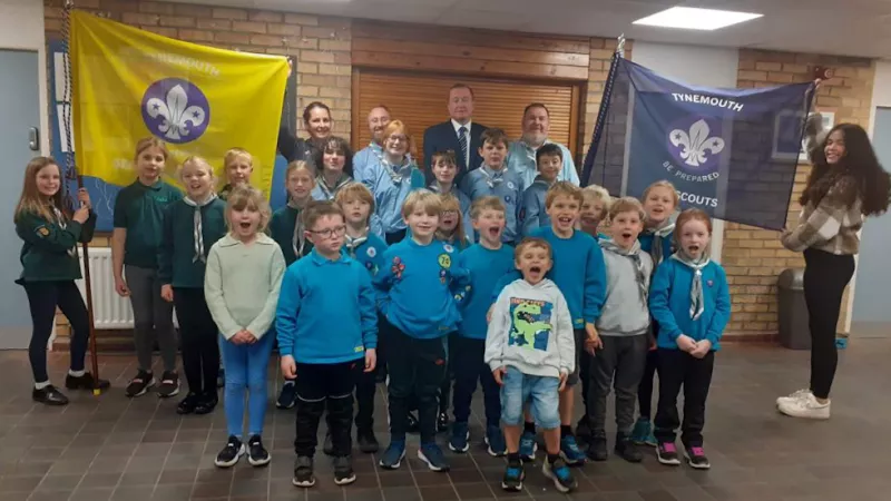 A group of Sea Scouts proudly holding up ther new banners. The banners are two flags, one yellow, one blue. Bother have the Sea Scouts logo on.