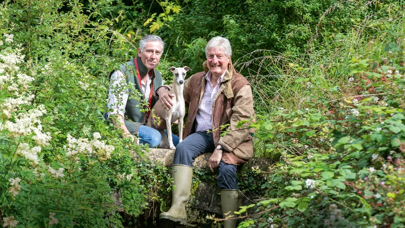 Tony and Tony2 with their dog sat surrounded by greenery